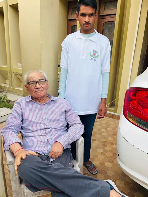 Caregiver standing behind a seated elderly man in a courtyard