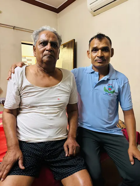 Caregiver and an elderly man seated together and smiling at the camera