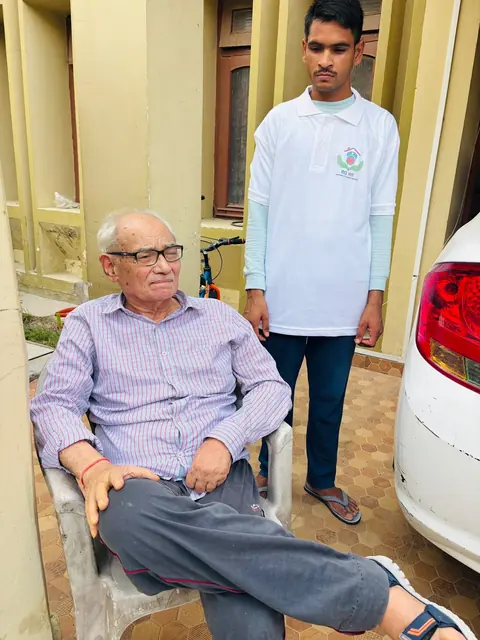 Caregiver standing next to a seated elderly man in a courtyard