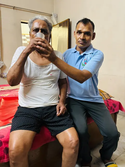 Caregiver helping an elderly man drink water while sitting together